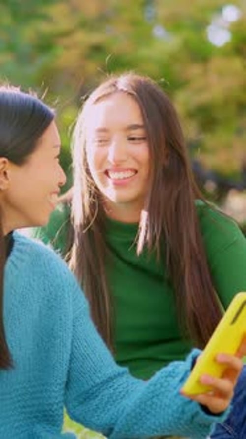 Smiling Young Women Looking at a Phone in Park