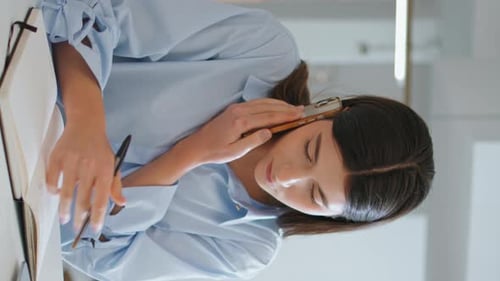 Woman Talking on Phone and Writing at Desk