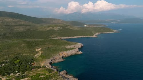 Drone view of a rocky shore by the Adriatic blue sea with mountains in the background, Greece, Croat