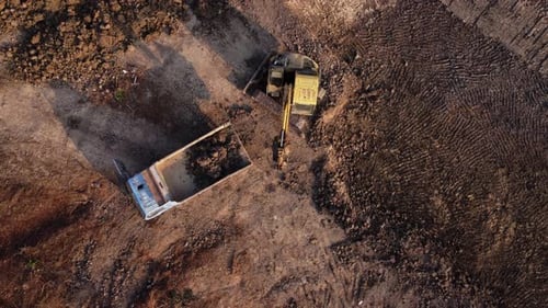 Aerial view of a wheel loader excavator with a backhoe loading sand into a heavy earthmover