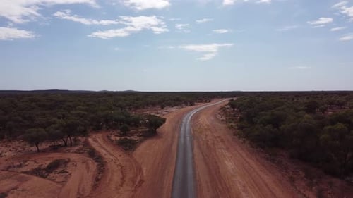 Drone ascending over a very remote country road surrounded with red soil and trees in the Australian