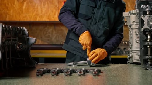 Closeup At a Service Station on the Table Young Engine Repairman Assembles a New Piston Part