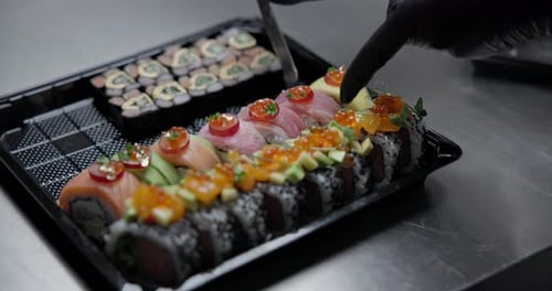 Ein Koch in schwarzen Handschuhen bereitet Sushi zu und legt die fertigen Lachsrollen auf eine Plastikschale