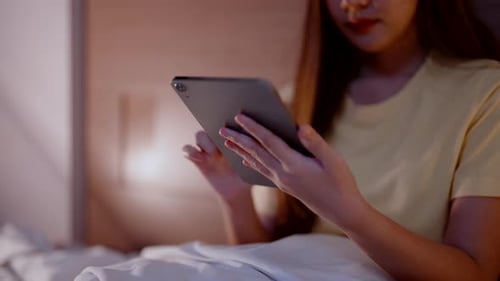 Evening environment in the bedroom of a young Asian woman, closeup of a woman's hand using a tablet.