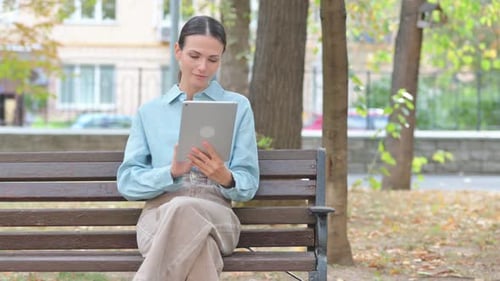 Woman Uses Tablet Sitting on a Park Bench