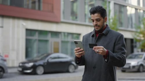 Man Uses Phone and Credit Card on Urban Street