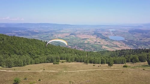 Paraglider flying close to the ground, slow flight above forest. Woman with yellow parachute in clos