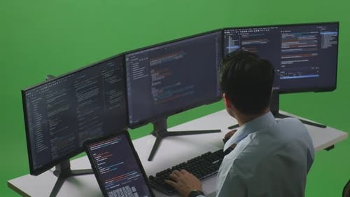 Asian Man Working With Tablet While Write Code With Multiple Computer Screens In Green Screen