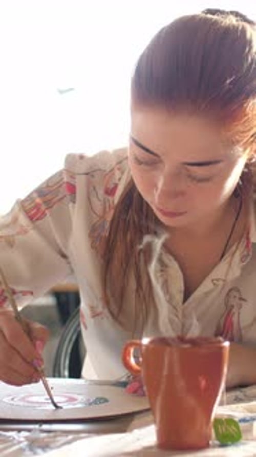 Young Woman Painting with a Hot Drink Nearby