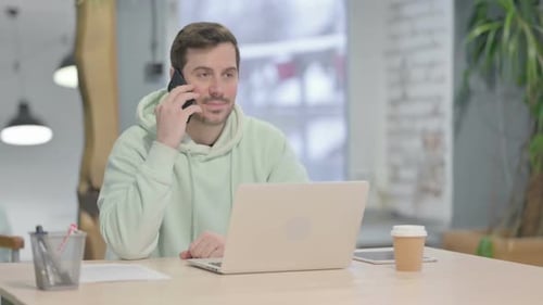Young Man Talking on Phone While Using Laptop