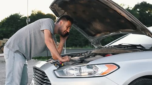 Man looks under the open hood of car