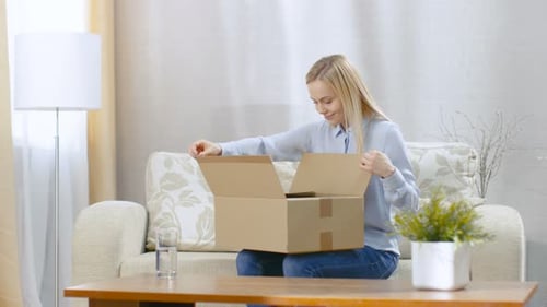 Woman Sitting on Couch Opening Cardboard Box