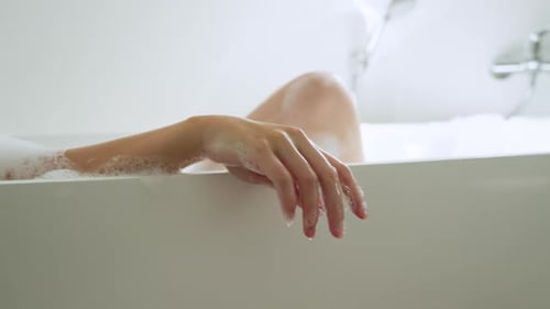 Mulher de spa reclinada em banho de espuma sobre toalha, movendo e estendendo o braço, formando gotículas para relaxar