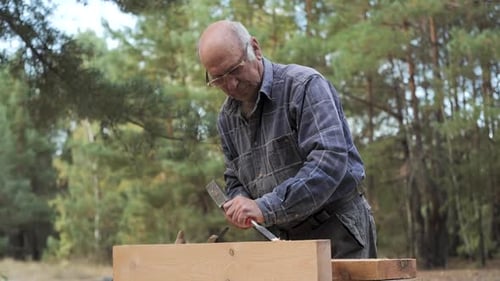An Elderly Craftsman Skillfully Processes Wood Using a Chisel and a Hammer