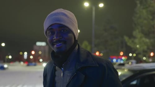 Smiling Man in Winter Hat Outdoors at Night with City Lights