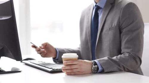 Businessman with smartphone enjoys morning coffee at his office workplace