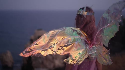 Back View Shining Wings on Fairy Costume of Caucasian Woman Standing on Night Cliff Looking Away at