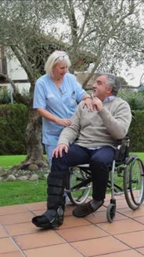 vertical Nurse assisting elderly man in wheelchair in a garden