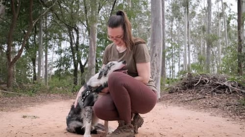 Woman with glasses having a nice time with her pet in a forest, Australian shepherd dog, caresses hi