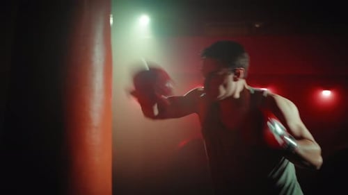 Man Boxing Punching Bag in Dark Gym
