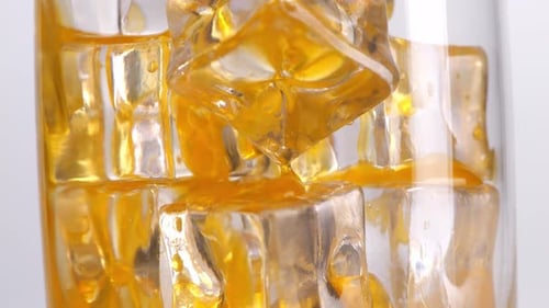 Close Up Of Orange Juice Being Poured Into A Glass With Ice Cubes On White Background