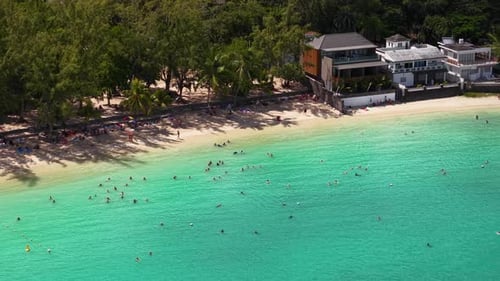 Aerial Drone View of Tourists Enjoying a Sunny Day at a Crowded Beach with Clear Turquoise Water