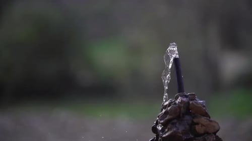 Foto de perto de uma pequena fonte de água espirrando água durante o dia e a floresta ao fundo. Lento m