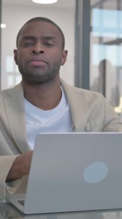 African Businessman Looking at Camera while Working on Laptop in Office, vertical video