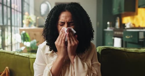 Woman with Curly Hair Sits on Couch and Sneezes