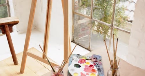 Easel with colorful abstract painting near window in cozy art studio, at home