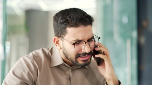 Angry dissatisfied businessman arguing talking on smartphone sitting at workplace in business office