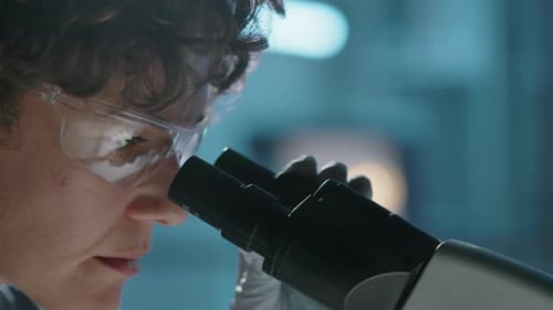 Gesicht einer Forscherin mit Brille, die im Labor in die Mikroskoplinse schaut