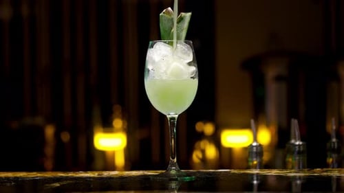 crystal glass filled with ice and decorated by aloe vera leaves being filled with a green alcoholic