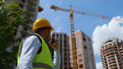 Nahaufnahme eines gutaussehenden männlichen Arbeiters mit Schutzhelm, der in Walkietalkie spricht, der auf der Baustelle steht