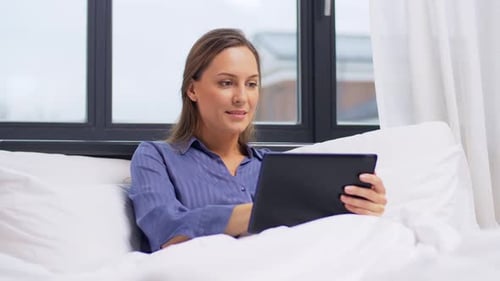 Woman relaxing in bed using a tablet computer
