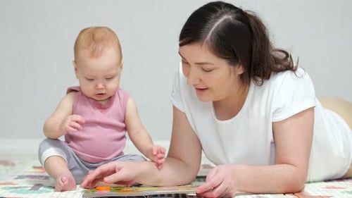 Mother and Baby Playing with Book on Mat