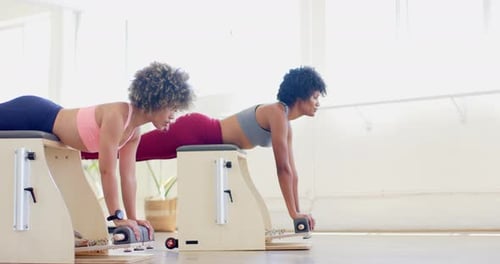 Mujer birracial y joven birracial haciendo ejercicio en un gimnasio luminoso con una silla de Pilates