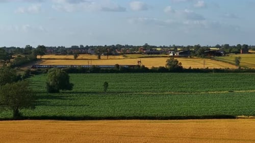 Personenzug fährt durch Ackerland mit Green and Golden Fields Pendler Rail Crossing Rural