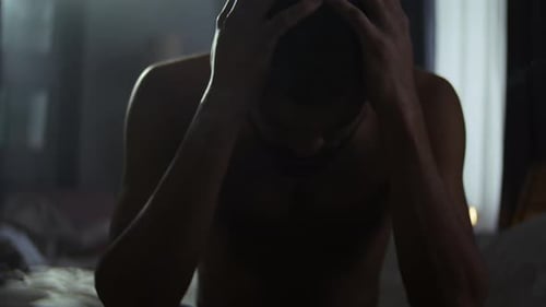 Distressed Man Sitting on Bed With Head in Hands