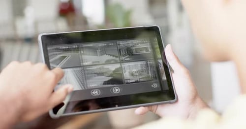Hands of biracial man using tablet with home security camera views on screen, slow motion