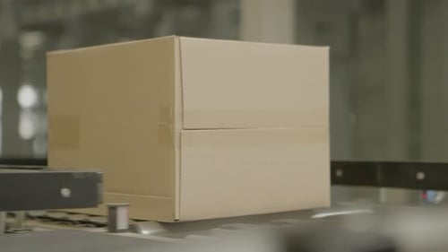 Cardboard box moving on a conveyor belt in a factory setting during daytime