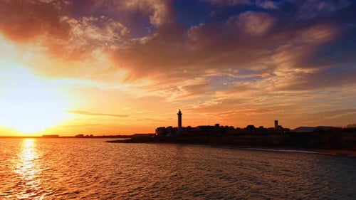 Scenic view of the sunset over the seascape. City skyline with lighthouse on the rocky shore.
