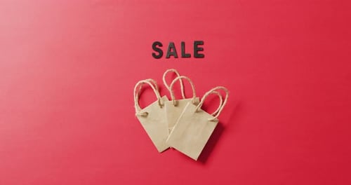 Sale in black letters with three brown gift bags on red background with copy space