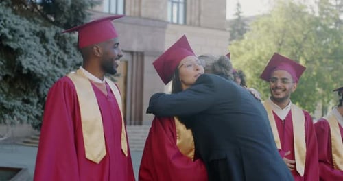 Proud Professor Congratulating Diverse Group of Students in Graduation Hats and Gowns Outside