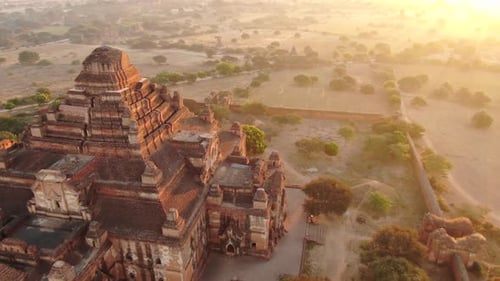 Ancient Buddhist temple in Bagan, Myanmar with dozens of hot air balloons in background during sunri