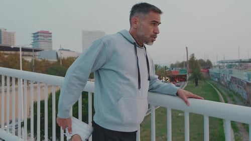 Middle aged man in sportswear stretching while standing on bridge before jogging