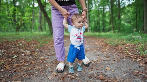 Little toddler stepping slowly looking around. Mommy’s holding her baby helping him to walk.