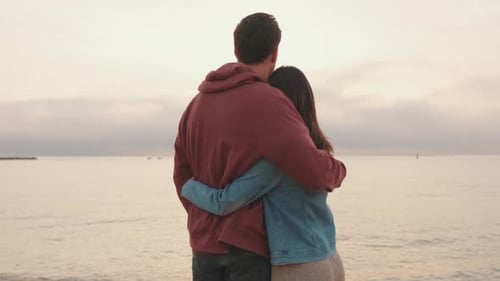Young couple standing embracing on seascape background.Back view