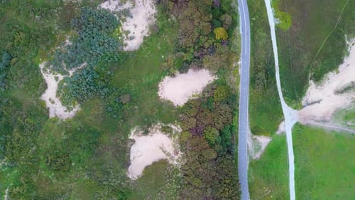 Aerial view of a coastal landscape with lush greenery, sandy dunes, and a winding road running