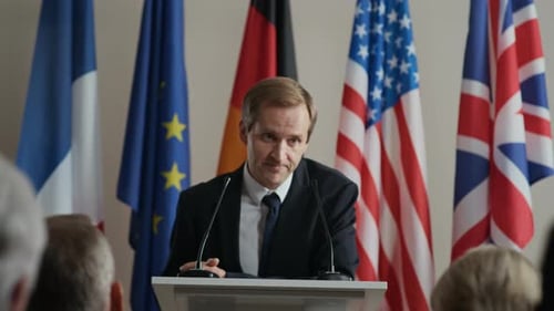 Man Speaks at Podium in Front of Flags